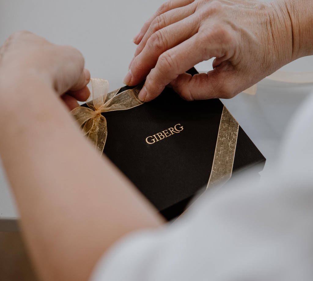 Hände verpacken eine elegante schwarze Geschenkbox als Firmengeschenk vom Schloss-Beck.
